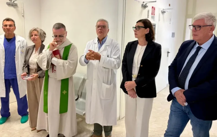 Sacerdote con stola verde, medici in camice e autorità nel corridoio della nuova area di osservazione dell'ospedale di Modica