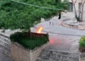 Fiamme su una panchina in pietra accanto a un'aiuola nella piazzetta Sacro Cuore di Comiso, con due persone sullo sfondo
