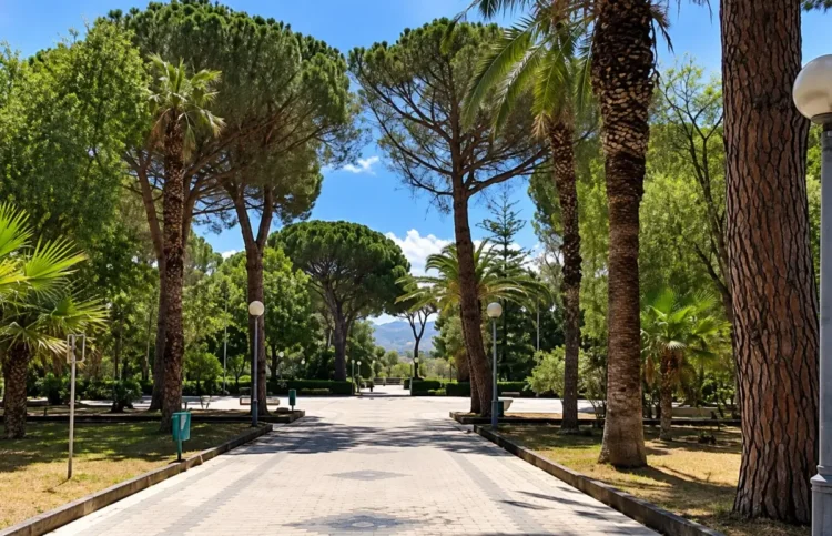 Viale lastricato della villa comunale tra pini, palme e lampioni sotto un cielo sereno. Immagine generata con intelligenza artificiale