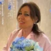 Patrizia Burrafato, ex presidente del Consiglio comunale di Pozzallo, sorridente con un mazzo di fiori azzurri e camicia rosa