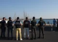 Agenti di Polizia, Polizia Scientifica e Guardia di Finanza di spalle su una banchina portuale, davanti a barche a vela