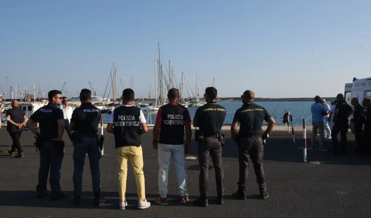 Agenti di Polizia, Polizia Scientifica e Guardia di Finanza di spalle su una banchina portuale, davanti a barche a vela