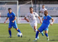 Due calciatori in maglia blu e uno in maglia bianca si contendono il pallone su un campo in sintetico durante Praia-Modica