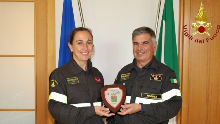 Una vigile del fuoco e il comandante dei vigili del fuoco di Ragusa reggono un crest davanti alle bandiere italiana ed europea