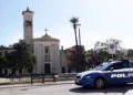 Auto della Polizia di Stato ferma in una piazza di Vittoria, davanti a una chiesa con campanile, palme e panchine