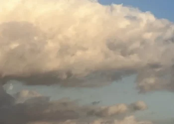 Grande nuvola bianca illuminata dal sole su un cielo azzurro, con nubi più scure nella parte bassa dell'immagine