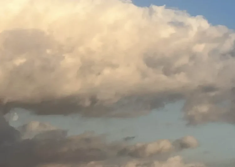 Grande nuvola bianca illuminata dal sole su un cielo azzurro, con nubi più scure nella parte bassa dell'immagine