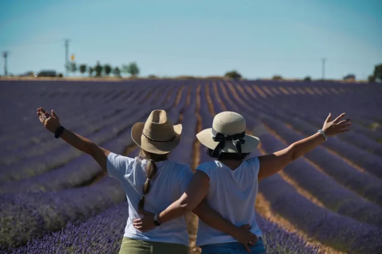 Due donne di spalle con cappello di paglia, abbracciate e a braccia aperte in un campo di lavanda: simbolo del reddito di libertà