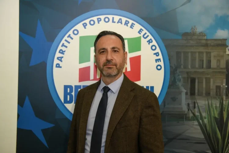 Biagio Pelligra, consigliere comunale di Forza Italia a Vittoria, in giacca marrone e cravatta davanti al logo del partito