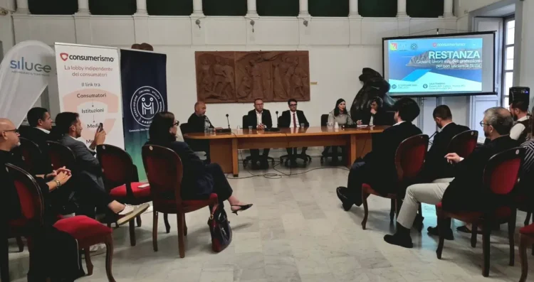 Relatori al tavolo del convegno Restanza a Modica, pubblico in sala e titolo dell’incontro proiettato sullo schermo