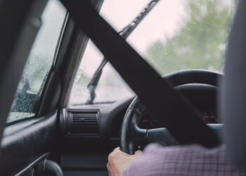 Automobilista al volante con la cintura di sicurezza allacciata, tergicristallo e gocce di pioggia sul parabrezza