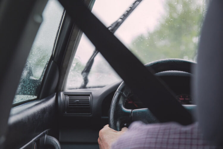 Automobilista al volante con la cintura di sicurezza allacciata, tergicristallo e gocce di pioggia sul parabrezza
