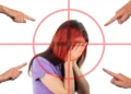 Ragazza con il volto coperto dalle mani dentro un mirino rosso, indicata da quattro dita: lo stigma sulla salute mentale