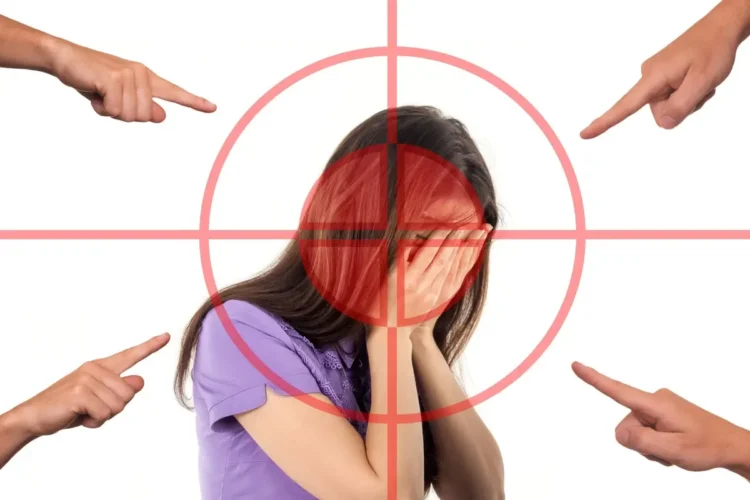 Ragazza con il volto coperto dalle mani dentro un mirino rosso, indicata da quattro dita: lo stigma sulla salute mentale