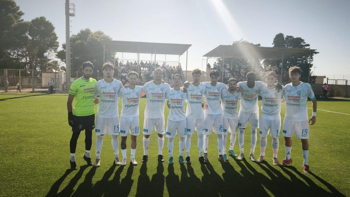 Giocatori del Santa Croce Soccer in maglia bianca schierati in campo con il portiere in verde, tribuna coperta sullo sfondo