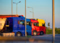 Camion di autotrasportatori parcheggiati in fila in un piazzale al tramonto, con motrici blu, rossa e gialla