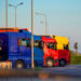 Camion di autotrasportatori parcheggiati in fila in un piazzale al tramonto, con motrici blu, rossa e gialla