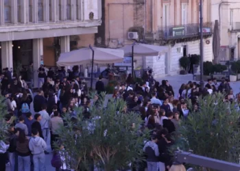 Studenti in sciopero a Ragusa radunati in piazza San Giovanni, tra gli ombrelloni di un bar e piante in primo piano
