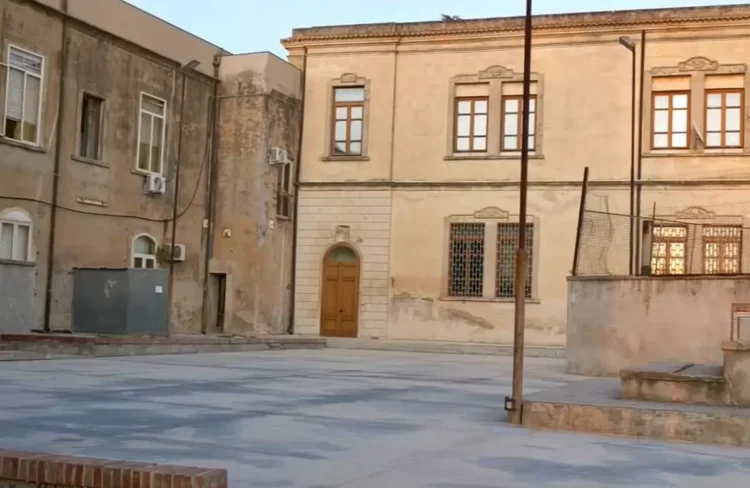 Cortile pavimentato con gradini e muretti tra due edifici storici a Chiaramonte Gulfi, scuole al centro delle critiche