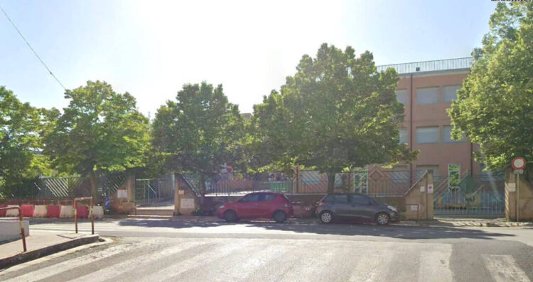 Scuola Palazzello a Ragusa: edificio rosa a tre piani dietro alberi e cancellata, auto parcheggiate e strisce pedonali