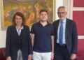 Uno studente con polo blu sorride tra un uomo e una donna in un ufficio, davanti a un dipinto con scene di mietitura