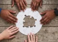Mani di giovani uniscono i pezzi di un puzzle circolare su un tavolo di legno, immagine simbolica del servizio civile