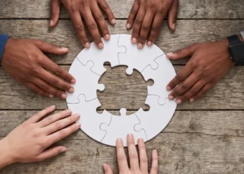 Mani di giovani uniscono i pezzi di un puzzle circolare su un tavolo di legno, immagine simbolica del servizio civile