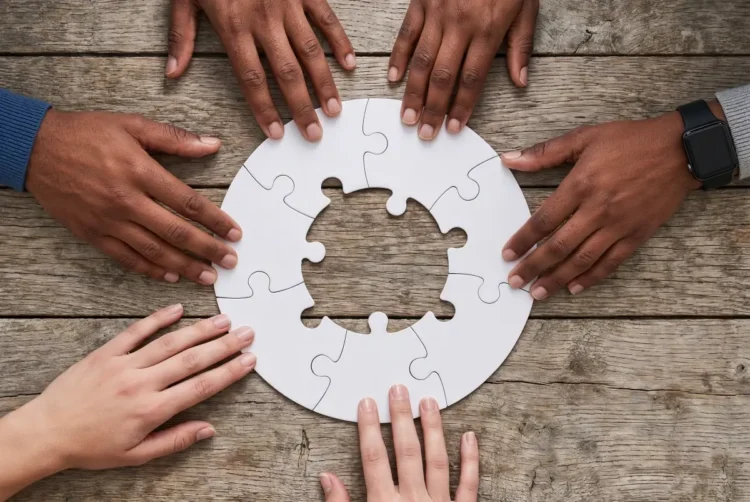 Mani di giovani uniscono i pezzi di un puzzle circolare su un tavolo di legno, immagine simbolica del servizio civile