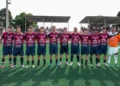 Undici giocatori del Frigintini in maglia rossoblu schierati a centrocampo prima della partita, portiere in arancione