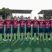 Undici giocatori del Frigintini in maglia rossoblu schierati a centrocampo prima della partita, portiere in arancione