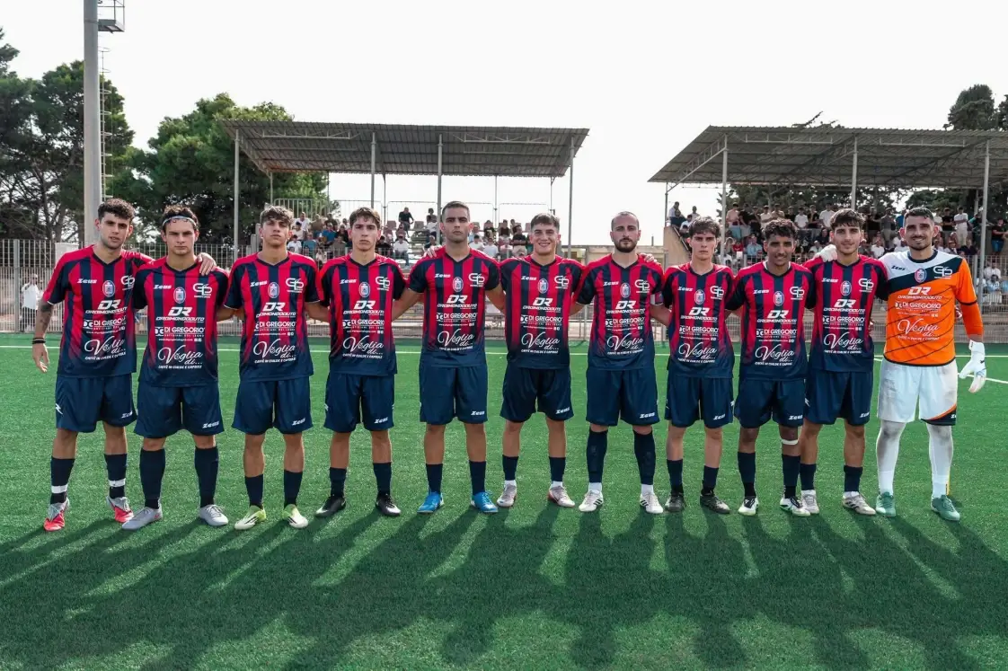 Undici giocatori del Frigintini in maglia rossoblu schierati a centrocampo prima della partita, portiere in arancione