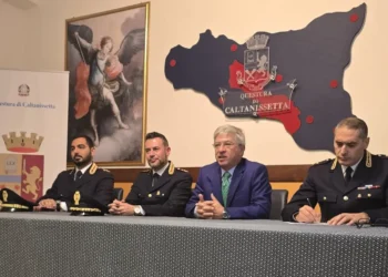 Funzionari in divisa e un uomo in giacca blu al tavolo della conferenza stampa nella Questura di Caltanissetta