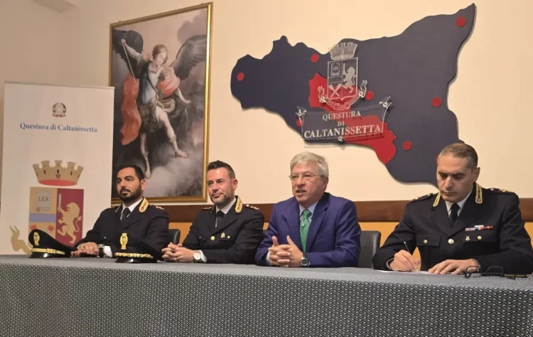 Funzionari in divisa e un uomo in giacca blu al tavolo della conferenza stampa nella Questura di Caltanissetta