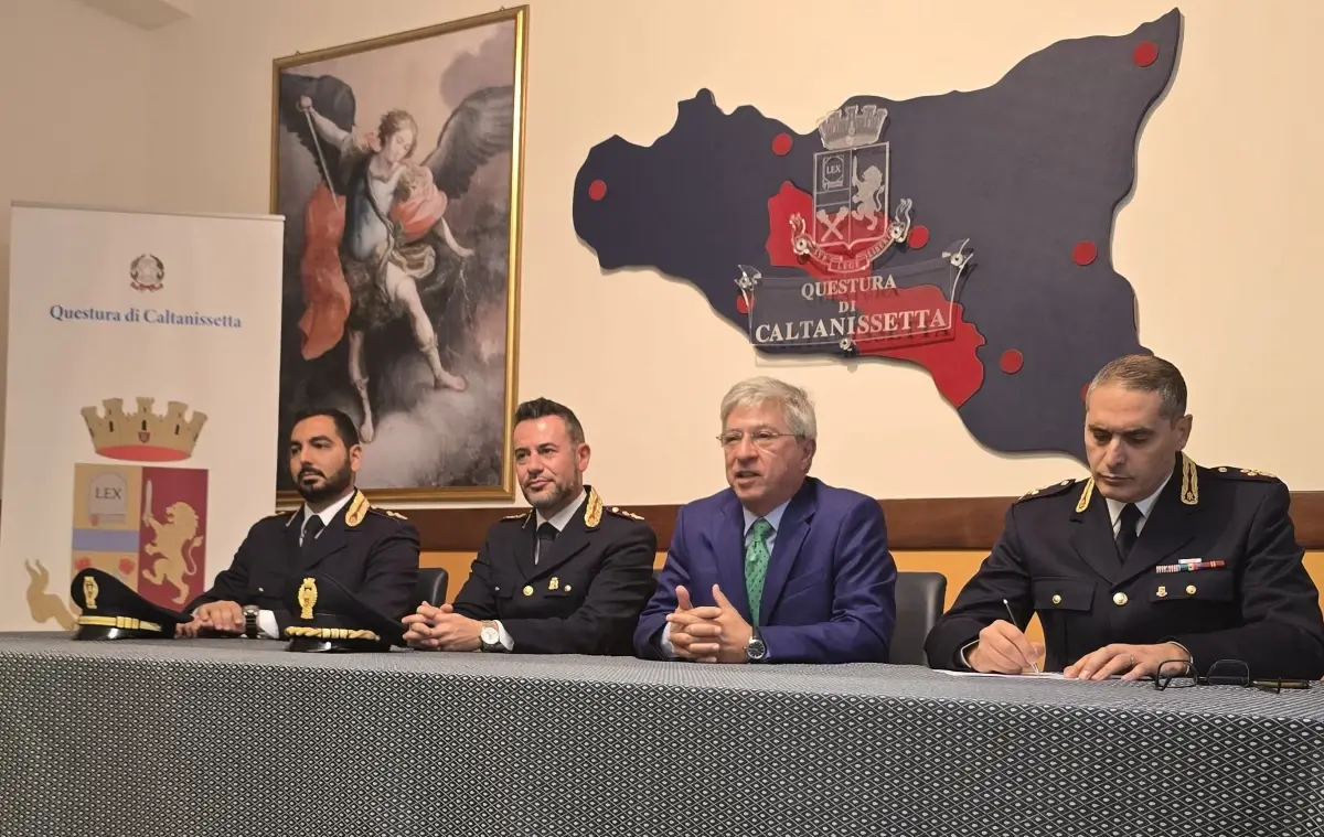 Funzionari in divisa e un uomo in giacca blu al tavolo della conferenza stampa nella Questura di Caltanissetta