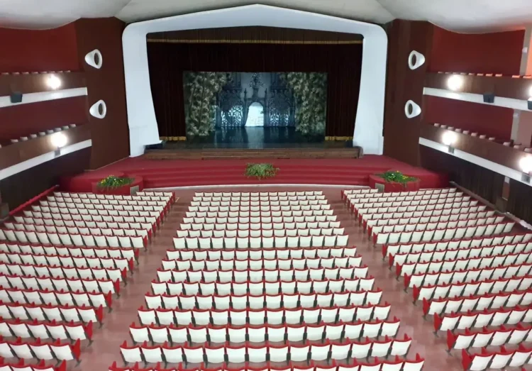 Platea del Teatro Duemila di Ragusa con poltrone rosse e bianche, balconate laterali e palco con sipario rosso aperto