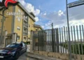 Auto dei carabinieri parcheggiata davanti al cancello di una caserma, con un palazzo giallo e il cartello «Carabinieri»