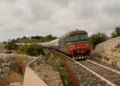 Treno storico con locomotiva diesel e carrozze d'epoca blu e crema in curva tra muretti a secco e macchia mediterranea