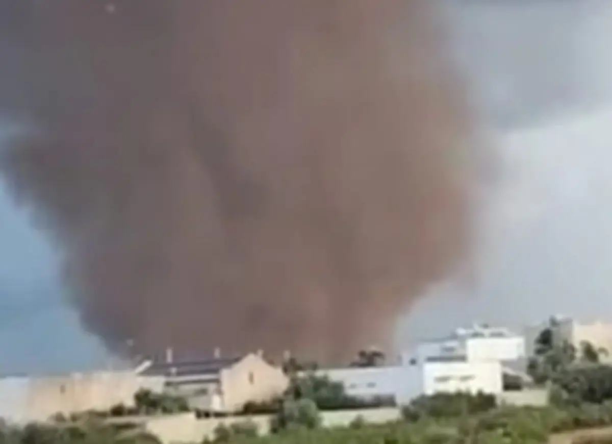 Tromba d’aria a Marsala: una colonna scura di polvere e detriti si alza dietro alcuni edifici bianchi, sotto un cielo grigio