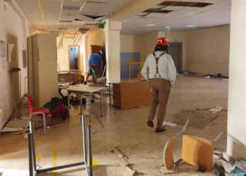 Controsoffitto crollato, arredi rovesciati e detriti in un edificio dopo le trombe marine; un uomo con casco ispeziona i locali