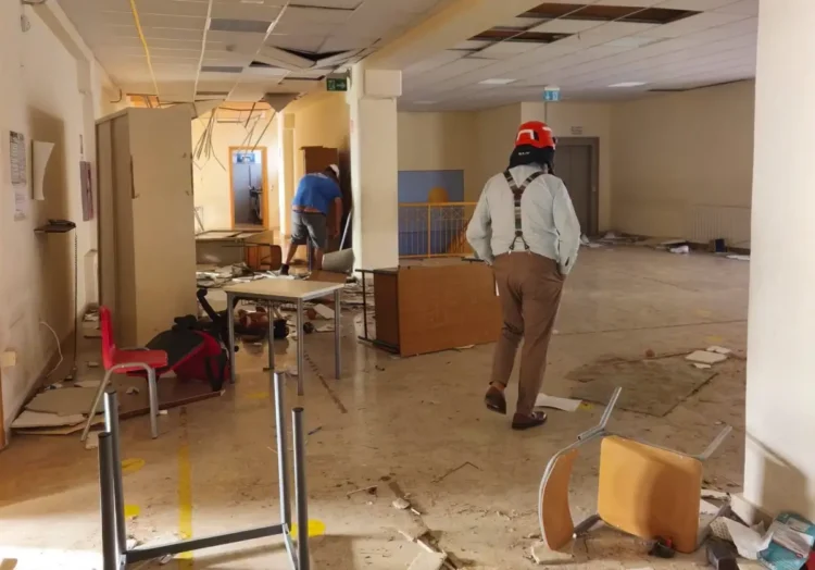 Controsoffitto crollato, arredi rovesciati e detriti in un edificio dopo le trombe marine; un uomo con casco ispeziona i locali