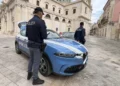 Due agenti della Polizia di Stato accanto a un'auto di servizio in una piazza lastricata davanti a una chiesa barocca