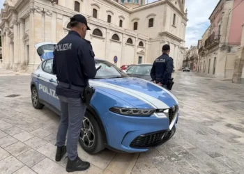Due agenti della Polizia di Stato accanto a un'auto di servizio in una piazza lastricata davanti a una chiesa barocca