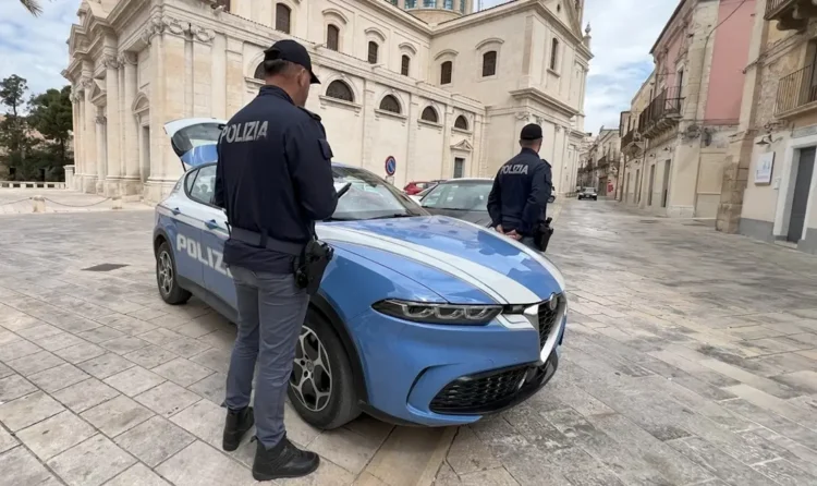 Due agenti della Polizia di Stato accanto a un'auto di servizio in una piazza lastricata davanti a una chiesa barocca