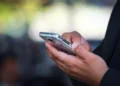 Mani di un uomo in giacca scura su uno smartphone, il canale usato nella truffa del finto sms della banca