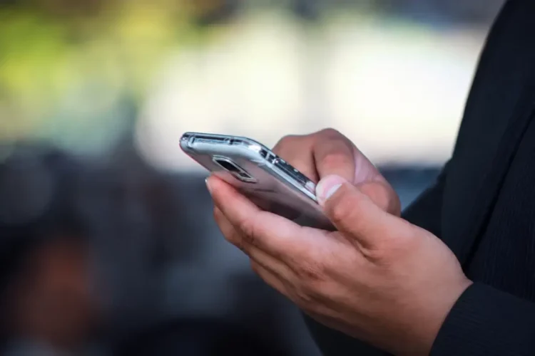 Mani di un uomo in giacca scura su uno smartphone, il canale usato nella truffa del finto sms della banca