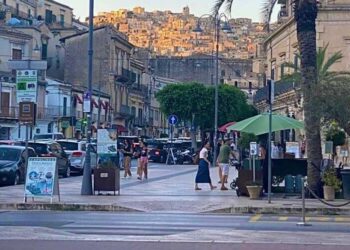 Turismo d’estate a Modica: passanti e tavolini all’aperto in centro, sullo sfondo le case di Modica Alta al tramonto