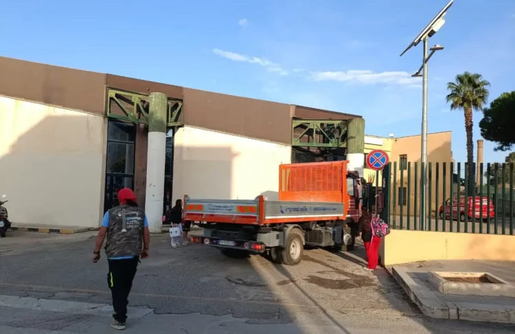 Camion di un’impresa davanti all’ingresso di una scuola a Vittoria, mentre alunni e un adulto arrivano a piedi